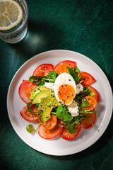Fresh salad with, tomatoes and boiled egg on white plate, healthy meal on dark green background