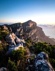 A breathtaking perspective of a rugged mountain vista under a clear, cloud-kissed sky during the golden hour, with the sea visible