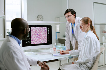 Multiethnic group of scientists analyzing microscopic image on computer monitor in laboratory,...