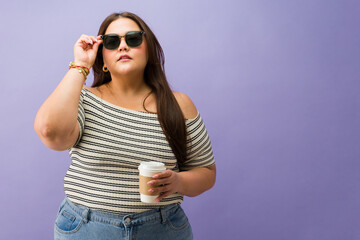 Fototapeta premium Curvy woman lifting sunglasses on purple background
