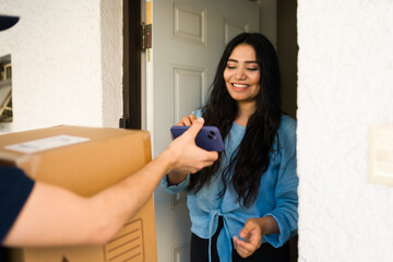 Smiling woman happily receives a package from a delivery person, signing for it on her mobile phone outside her residence