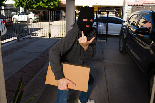 Porch pirate stealing delivery package from front steps and making an obscene gesture to camera