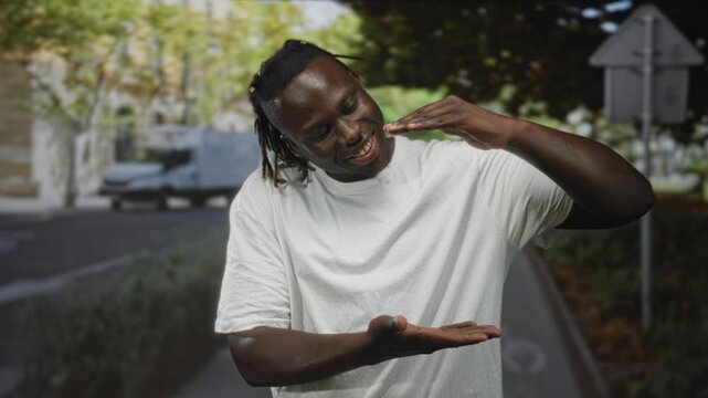 Man wearing white t shirt smiling with palms up presenting empty space on a city street; joyful play.