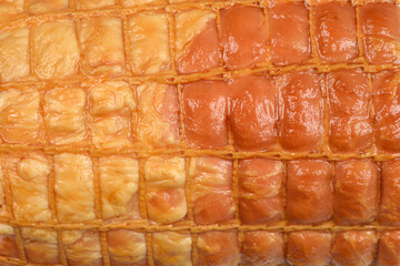 An extreme close-up, full-frame background of the golden-brown casing of a smoked meat roll, highlighting the intricate rectangular pattern created by the elastic netting