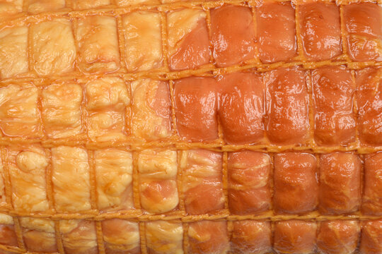 An extreme close-up, full-frame background of the golden-brown casing of a smoked meat roll, highlighting the intricate rectangular pattern created by the elastic netting