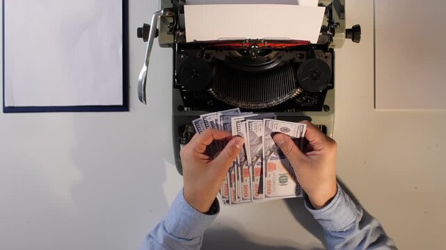 Hands counting pile of hundred dollar bills on a desk with an old vintage typewriter, symbolizing income from writing, publishing, or generating content