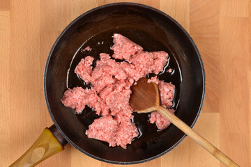 An overhead shot shows raw ground meat with a wooden spoon in a dark frying pan on a wooden cutting board, ready for cooking