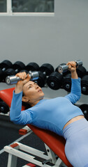 Close-up view of a fit Caucasian woman during gym workout. Bench press with dumbbells for chest. Gym scene shows woman performing bench press to tone chest and upper body.