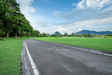 Empty asphalt road through green park with mountain landscape.