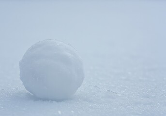 A close-up view of a perfectly spherical, hard snowball resting on fresh white snow, showing the frozen water crystals and cold winter texture ,cold ,icy ,hard