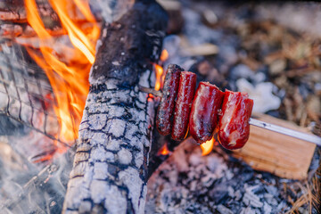 Grilled sausages on a skewer over an open fire, with vibrant flames and glowing embers creating a warm atmosphere, perfect for outdoor cooking and camping experiences