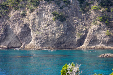 紺碧の海の上を行く３隻のカヤックと背後にそびえる海食によって削られた巨大な岩壁