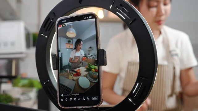 Smartphone screen showing an Asian food vlogger preparing ingredients, mounted on a ring light for a live stream