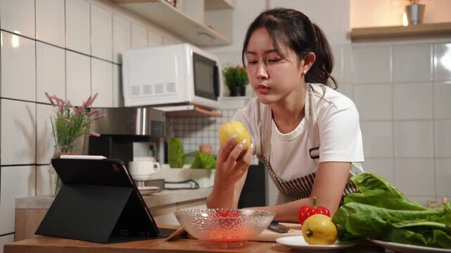 Focused Asian woman holding a lemon and checking a recipe or tutorial on her digital tablet while cooking in the kitchen