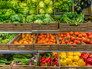 Vegetables displayed on supermarket shelves. Lettuce salads with tomatoes, peppers in crates displayed by greengrocer.