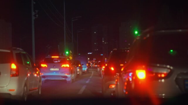 Cars are stuck in a traffic jam at night on a city road. The lights from vehicles create a colorful scene as drivers maneuver slowly through limited traffic