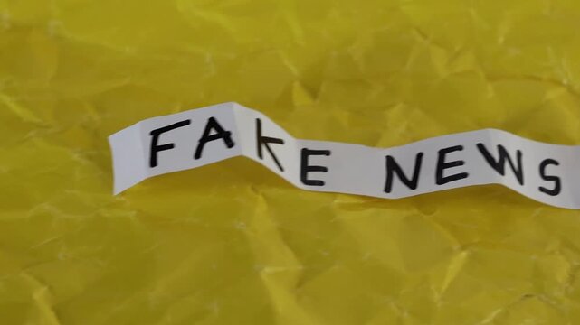 Un primer plano de un papel de color blanco con las palabras noticias falsas con en movimiento en un fondo amarillo