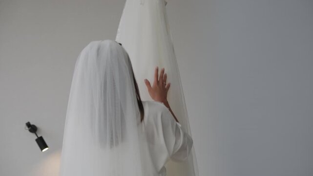Close-up of a bride in a vail touching gently a white satin wedding dress