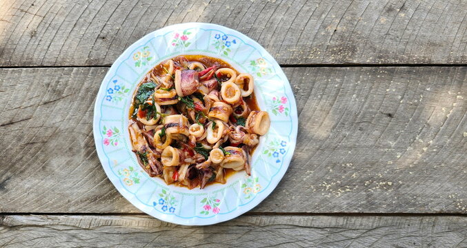 Stir fried Squid with basil : octopus or squid stir-fried in spicy flavorful sauce served on a floral plate. Spicy seafood served on a wooden table. Overhead shot of food squid in red curry paste 
