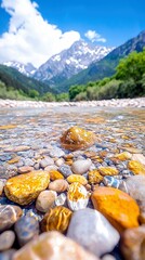 Close-up view of colorful, smooth pebbles submerged in a clear, shallow mountain stream. In the background, lush green trees line the banks, leading to majestic
