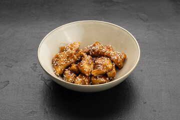 Sesame glazed chicken bites in a bowl on dark stone background