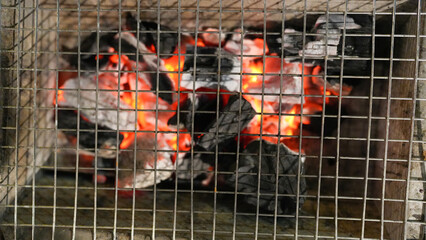 Glowing Charcoal Embers in a Wire Mesh Grill, Ready for Outdoor Cooking, Barbecue, or Campfire, Capturing the Warmth and Charred Texture of Grilling
