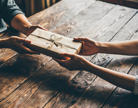 Hands exchanging a golden gift box on a wooden table in warm light