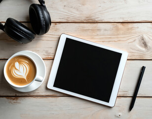 Minimal tech workspace arranged on light wood surface. Digital tablet with blank screen, black headphones, stylus pen, coffee cup with latte art present. Modern setup perfect for remote work, study,