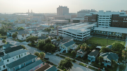 Tower port cranes, dense cluster of hospital, research buildings, residential houses stretch busy harbor, where ships, industrial facilities underscore Galveston coastal urban complexity, Texas