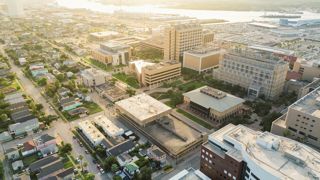 Parallel residential streets row of pastel homes with porches, parked cars lining, hospital buildings high-rise towers, illustrating community integration and zoning contrast in Galveston, Texas