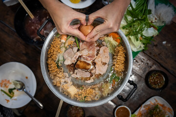 Sliced meat and vegetables cook in a metal grill pot filled with broth and steam, while the center grill browns the meat.