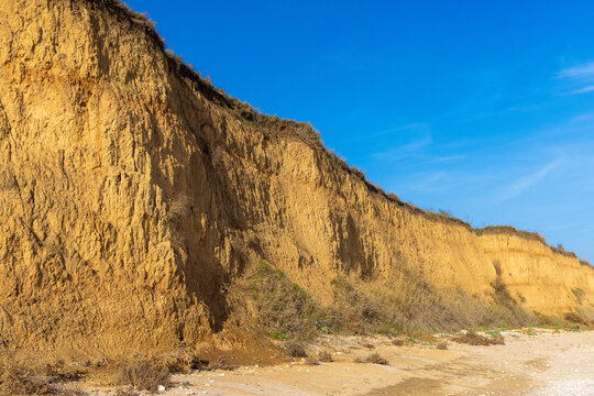 A steep, eroded cliff face composed primarily of sandy, yellowish clay soil