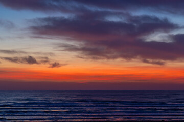 A scenic view of a dramatic sunset or sunrise over the ocean, with vivid orange, red, and purple hues reflecting on gentle waves