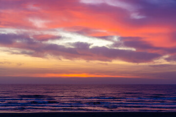 Landscape with a beautiful sunset over the ocean with vibrant colors, including deep reds, oranges, and purples, with dramatic clouds