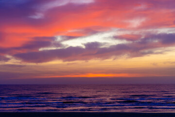 Obraz premium Landscape with a beautiful and vibrant sunset over the ocean, with the sky painted in various hues of orange, pink, purple, and yellow