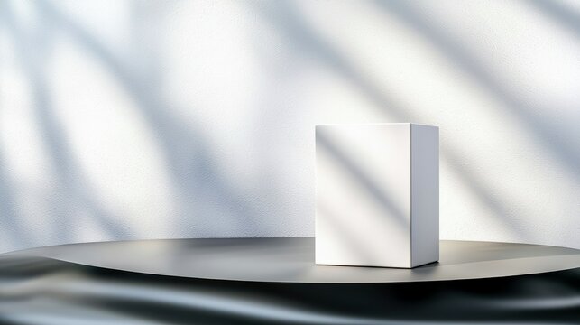 A minimalist composition featuring a clean white rectangular box placed on a dark, reflective, curved surface. The background is a textured white wall with dapp