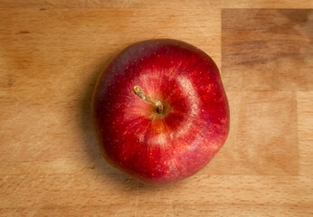 Overhead View of a Single Red Apple Centered on a Light Brown Wooden Cutting Board