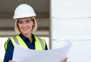 Confident female engineer in a hard hat holding a blueprint on a construction site. Professional woman architect smiling at the camera with copy space