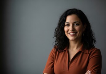 Smiling woman with dark curly hair and arms crossed against a gray background