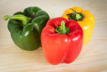 Trio of Ripe Bell Peppers (Red, Green, Yellow) Grouped Closely on a Light Wooden Background