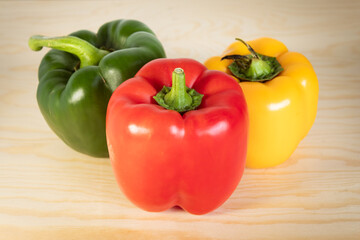 Colorful Bell Peppers (Red, Green, Yellow) Grouped on a Light Wood Surface in Studio Lighting