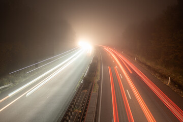 High angle long exposure shot of a foggy highway at night with intense bright white light from oncoming vehicles and receding red light streaks creating high contrast