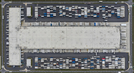 Aerial top view of a large warehouse and parking lot with rows of trucks and trailers, logistics and cargo hub, modern distribution center. Industrial commercial logistics concept.