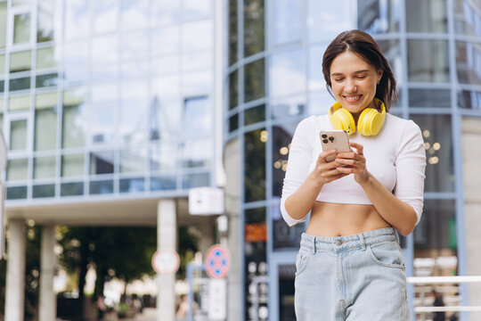 Young woman smiling using smartphone in urban setting - Powered by Adobe