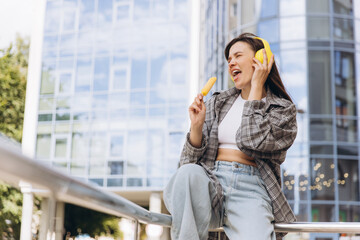 Fototapeta premium Woman singing with headphones and eating ice pop