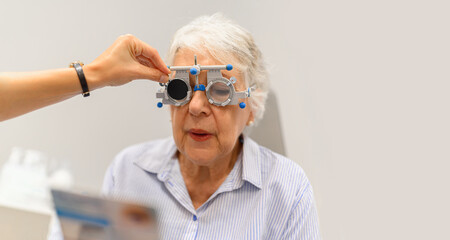 Female ophthalmologist's hand adjusting phoropter while senior woman reads eye chart during vision...