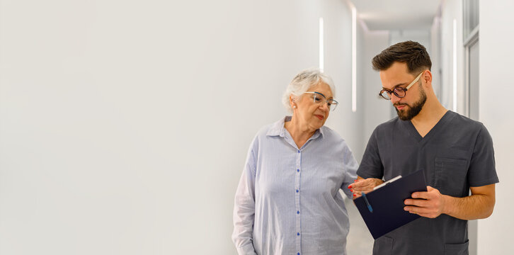 Male doctor discussing medical results with senior patient while walking through hospital corridor during routine checkup visit