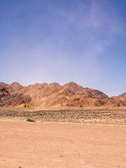 Red rocky desert detail with distant mountains and a wind blown cloud of dust