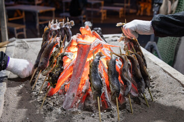 赤く燃え盛る炭火で塩焼きにされる串に刺さったイワナやヤマメ