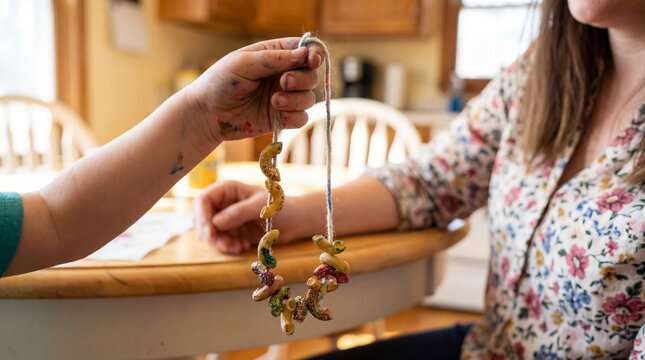 Child Presenting Homemade Pasta Noodle Necklace to Mother - Powered by Adobe